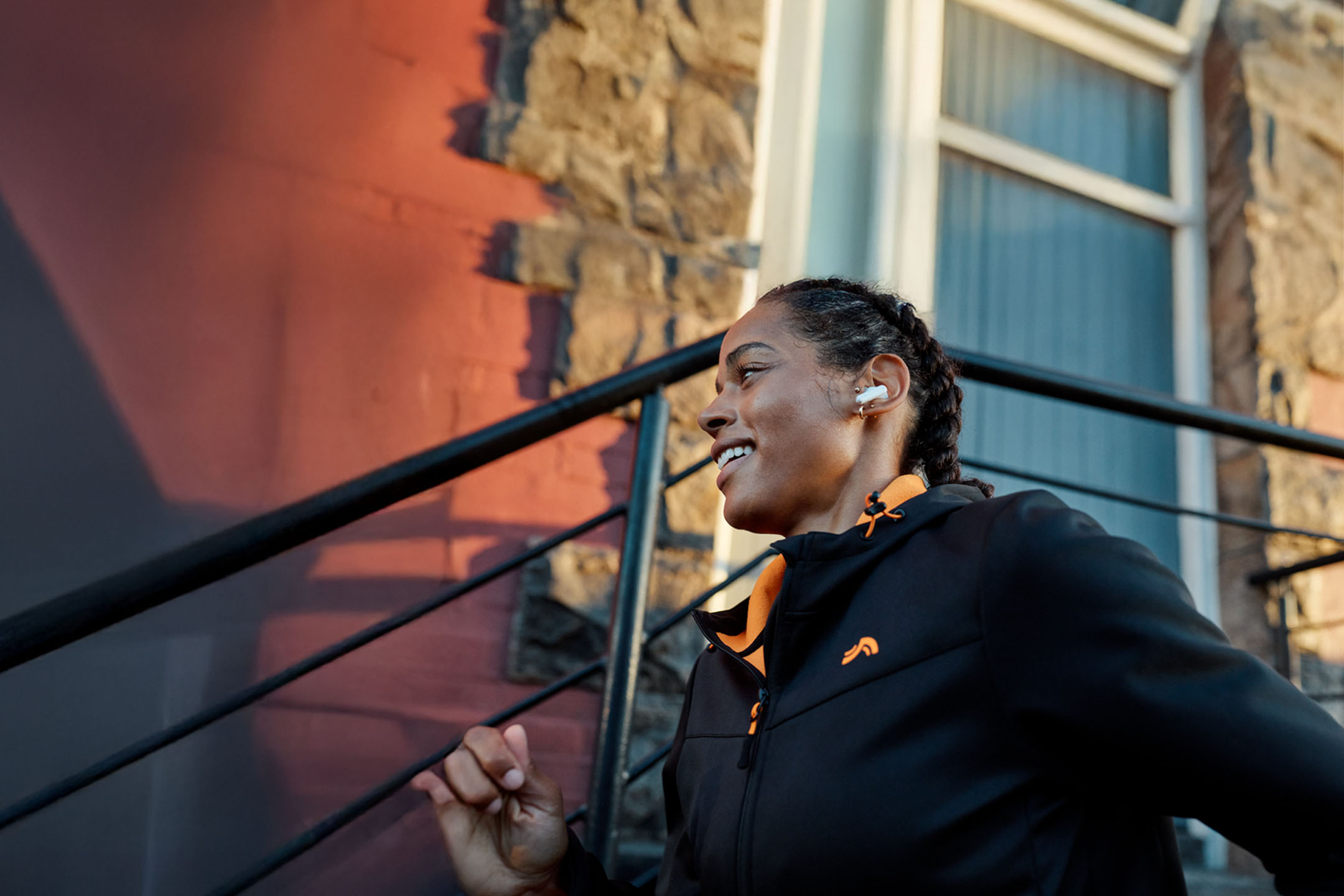 Kvinna joggar med hörlurar, bär jacka.