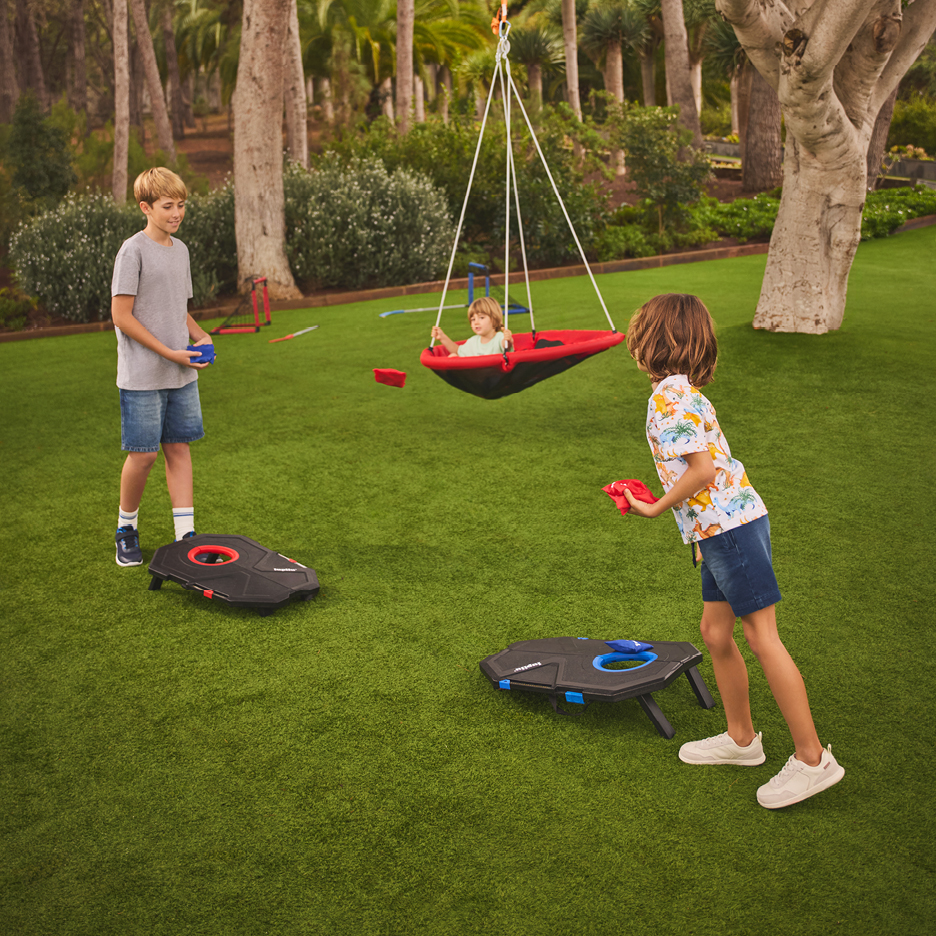 Barn leker med majskastningsspel och en gungsits i en trädgård.