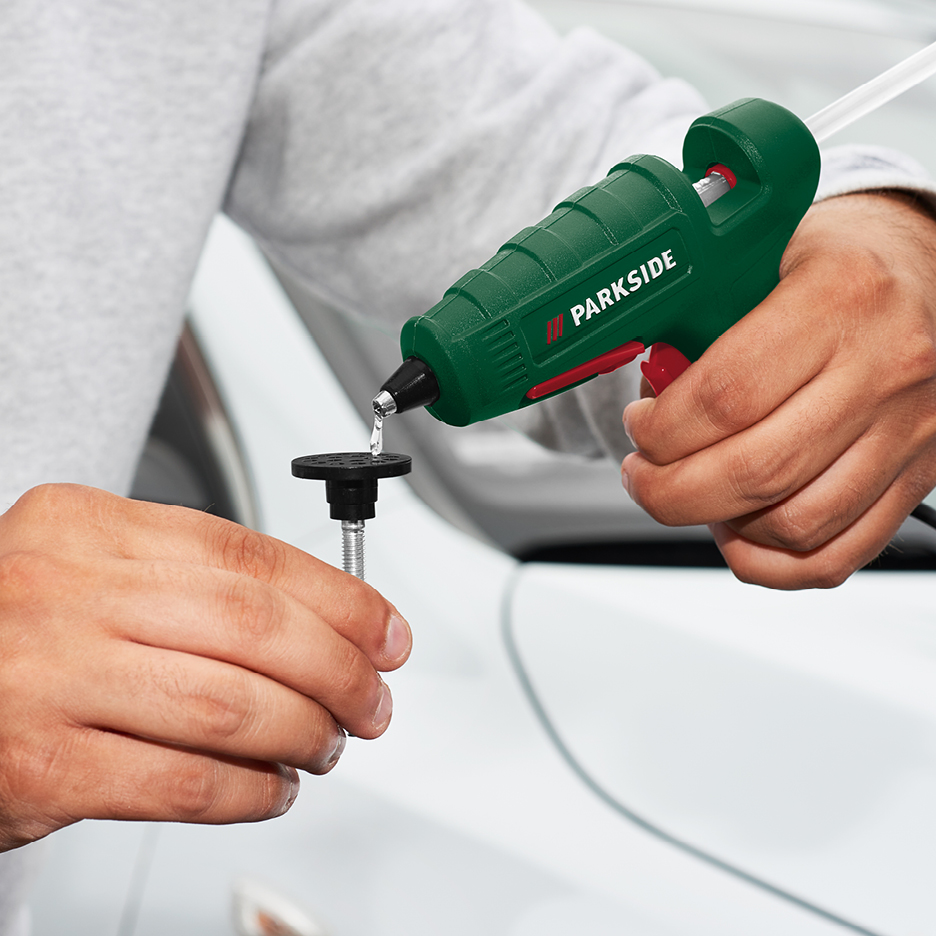 En person applicerar smältlim på en svart sugkopp med en limpistol för att reparera en bil.